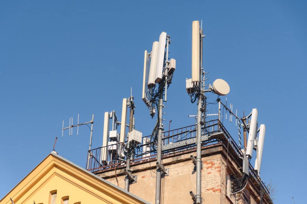 Cluster of mobile network broadcast cell repeaters on roof of building in city.